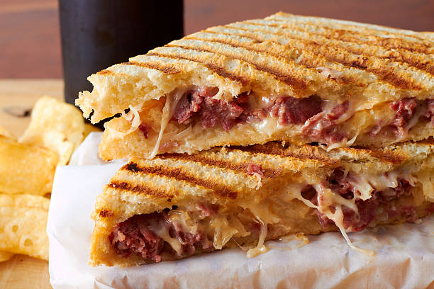 Grilled panini sandwich A gooey meat and cheese sandwich on wax paper with chips and a drink in the background. reuben sandwich stock pictures, royalty-free photos & images