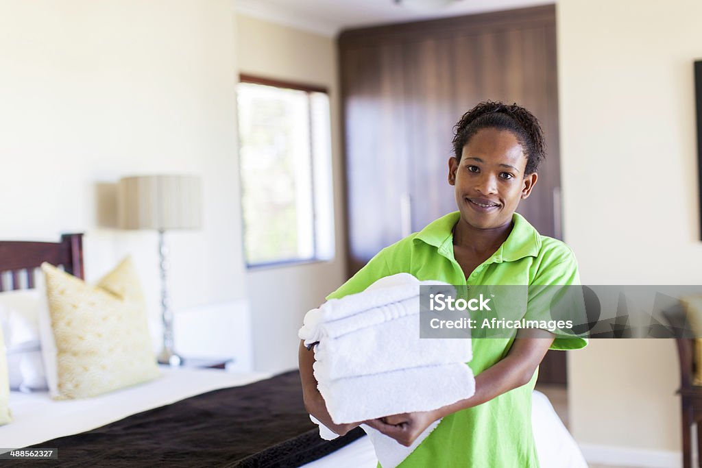 African housekeeper smiling at the camera African housekeeper looking at the camera holding a towels under her arms in a hotel room in Langebaan, Western Cape, South Africa Hotel Occupation Stock Photo