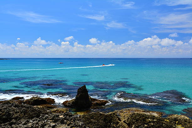 Brown and grey color coral reef at seashore. Blue sea and white spoondrift. A jet ski moved fast at far place. White clouds floating at blue sky, sunlight and sunny weather. Kenting,Taiwan Strait,Taiwan.