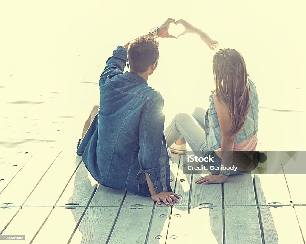 Love Couple sitting on the pier,their hands show heart Couple in love sitting on the pier, their hands show heart Couple - Relationship Stock Photo