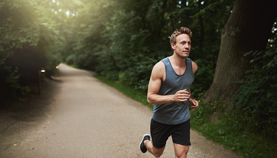 Active, fit and healthy man jogging on a beach while listening to music on earphones with stunning outdoor clear sky and sea copy space. Happy, mature and athletic guy running, doing fitness exercise