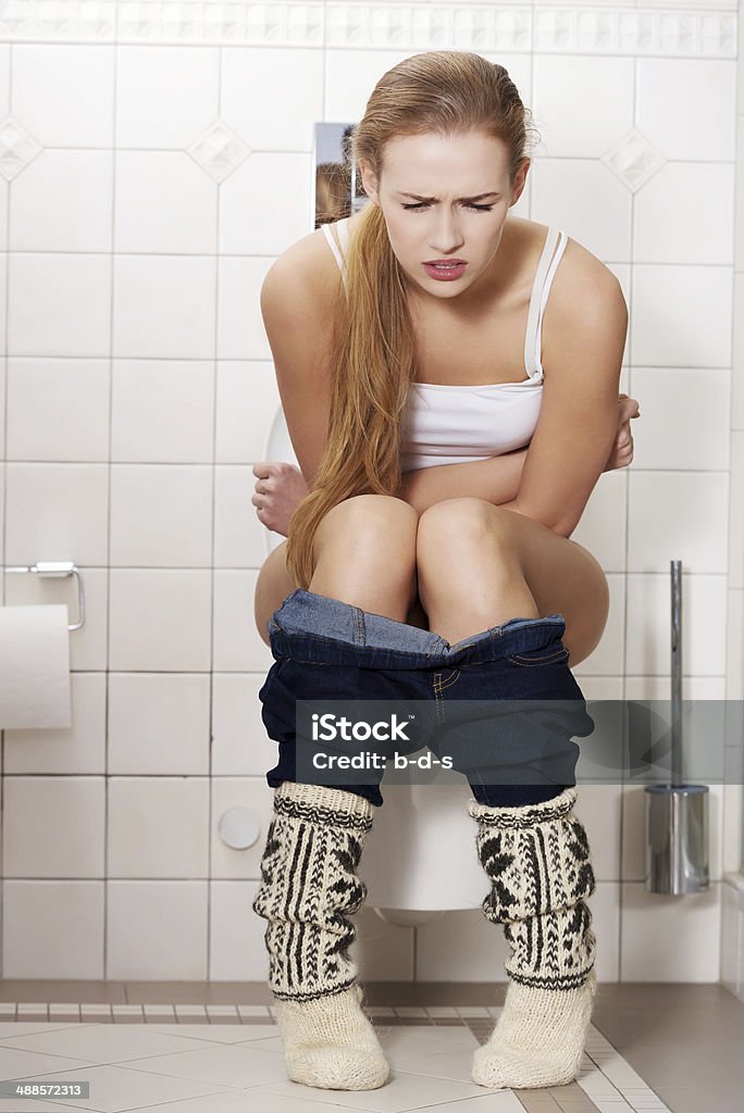 Young caucasian woman is sitting on the toilet. urinary bladder Young caucasian woman is sitting on the toilet. urinary bladder problem or pregnancy or sickness concept. Bathroom Stock Photo