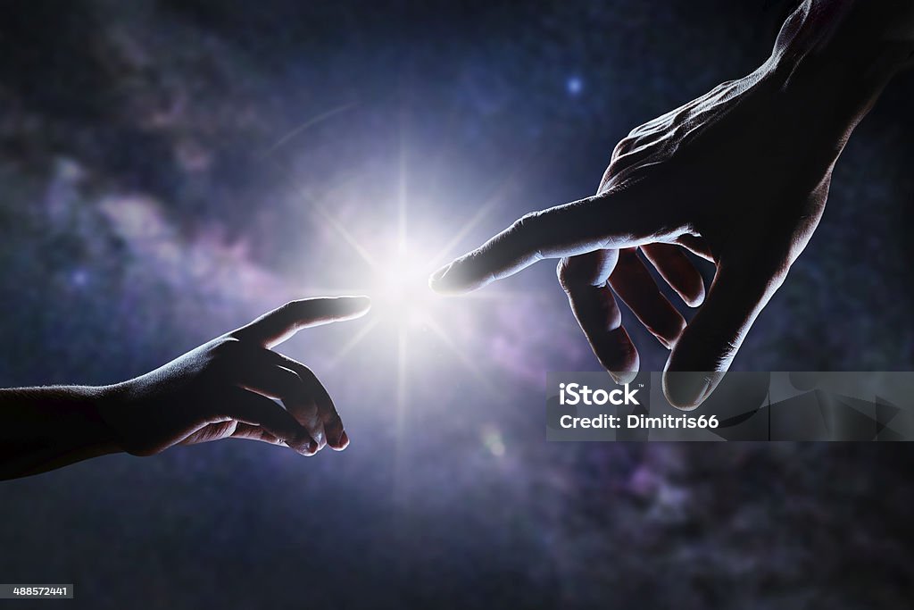 Hand Of God Close up of two hands, adult's and child's, reaching each other like Michelangelo's painting in front of stars and galaxy. Light is shining between father's and son's fingers. High contrast, lens flare. God Stock Photo