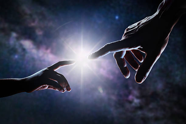 Hand Of God Close up of two hands, adult's and child's, reaching each other like Michelangelo's painting in front of stars and galaxy. Light is shining between father's and son's fingers. High contrast, lens flare. origins stock pictures, royalty-free photos & images
