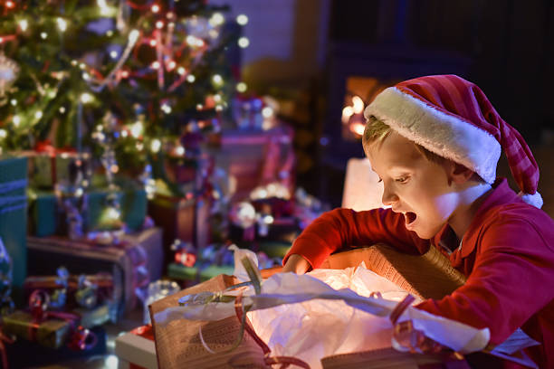istock christmastime, little boy opening a gift  near tree lit up 488574802