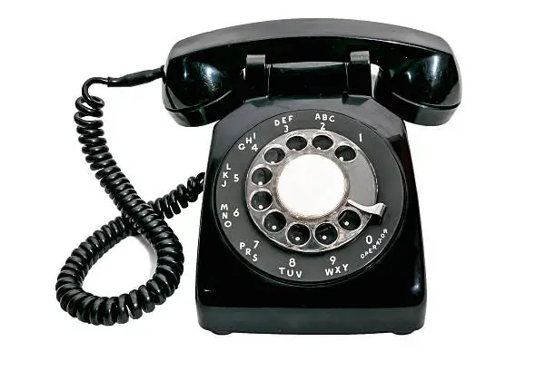 Close up shot of a black vintage rotary dial telephone isolated on a white background