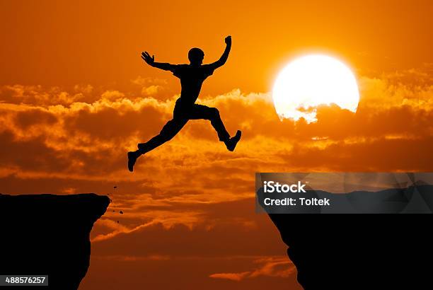 Man Jump Through The Gap Stock Photo - Download Image Now - Jumping, Mountain Peak, Sunset