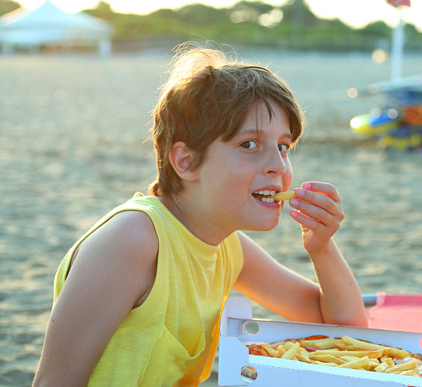 smiling boy eats pizza with potato chips on the beach at sunset