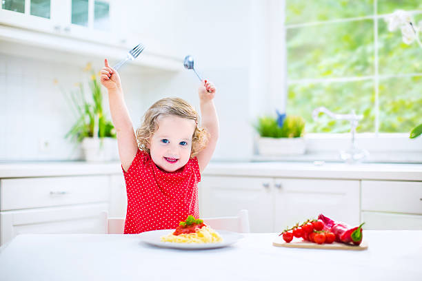 istock Cute toddler girl eating spaghetti in a white kitchen 488612085