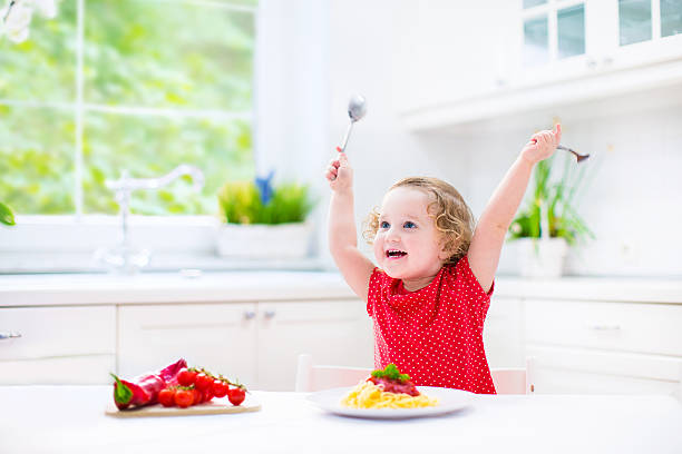 istock Cute laughing toddler girl with fork and spoon eating spaghetti 488612099