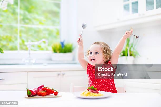 Cute Laughing Toddler Girl With Fork And Spoon Eating Spaghetti Stock Photo - Download Image Now