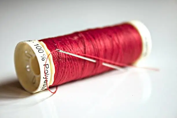 Red thread on gray background with a needle