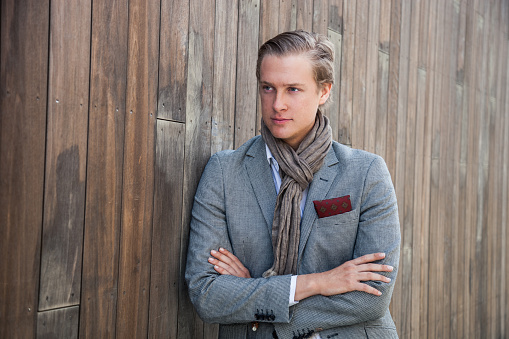 Casual young man posing on the wooden wall. He is wearing an elegant suit.