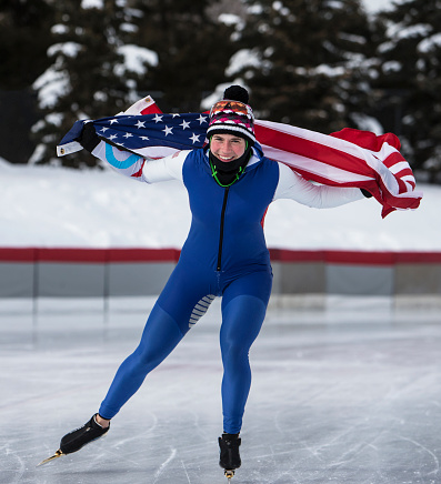 A female speed skater carrying the American flag while taking a victory lap around the ice rink.