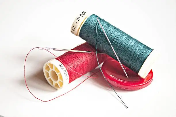 Red and green thread full on white background with needles and sewing item
