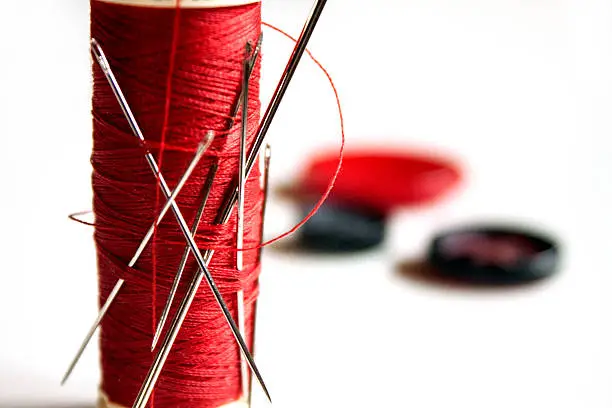 Red thread full of needles and sewing items on white background