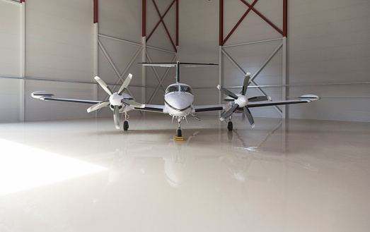 Small two-propeller aircraft parked in a big hangar