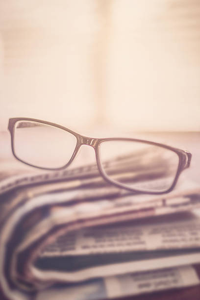 une pile de journaux et lunettes de vue dans la lumière - pile of newspapers flash photos et images de collection