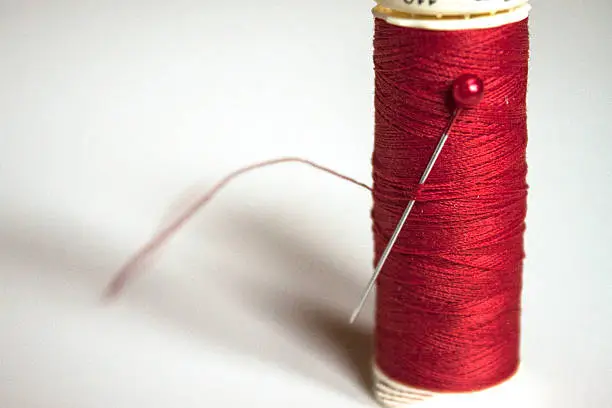 Red thread on gray background with a red pin