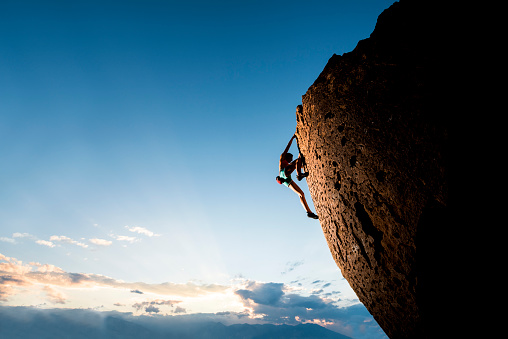 Strong female rock climber on a steep overhanging cliff at sunset