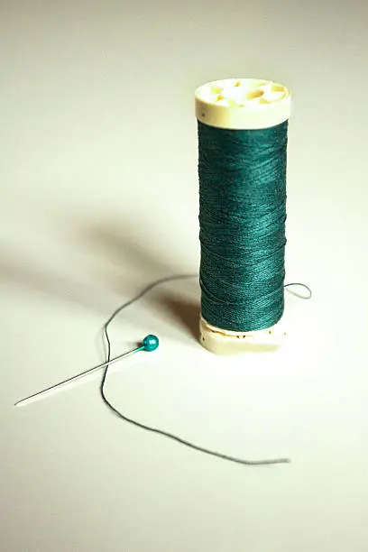 Green thread on gray backgrund with a green pin