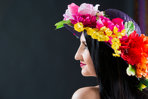 Young woman with long, black hair wearing hat, decorated with colorful flowers.