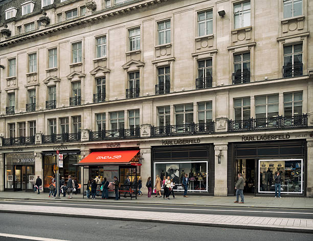 Shops in Regent Street, London London, England - September 8, 2015: People walking past some of the up-market shops in London’s Regent Street, while others wait at a bus stop. Regent Street is one of the West End of London’s major shopping streets and is very popular with tourists to the capital. It is a very long street, reaching from Langham Place to St James’s. (Overcast day.) karl lagerfeld stock pictures, royalty-free photos & images