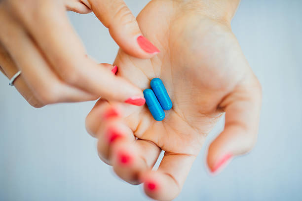 istock Women's fingers with pink manicure taking blue pills 488678534