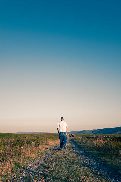 istock Man Walking alone on a remote country road 488679206