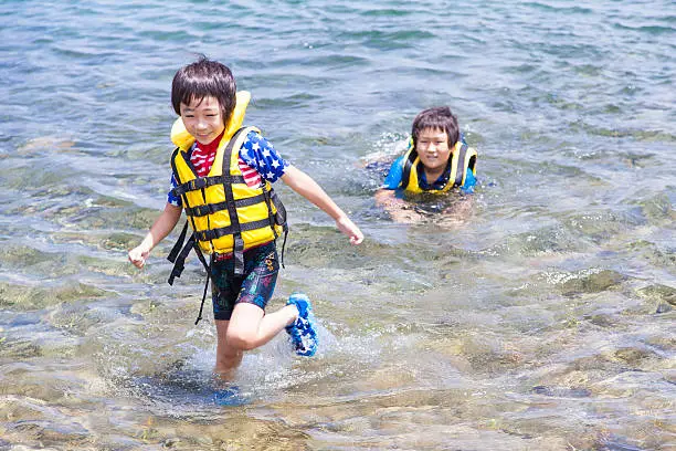 Asian boys wearing life jackets are playing in the lake.