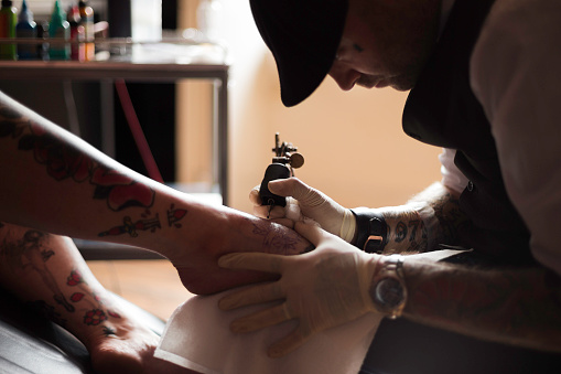 Close up shot of a male tattoo artist using a needle gun to tattoo a woman's foot.