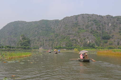Ninh Binh, Vietnam - October 11, 2014: People rowing boats for carrying tourists on Ngo Dong river of the Tam Coc National Park. Tam Coc is a popular tourist destination near the city of Ninh Binh in northern Vietnam.