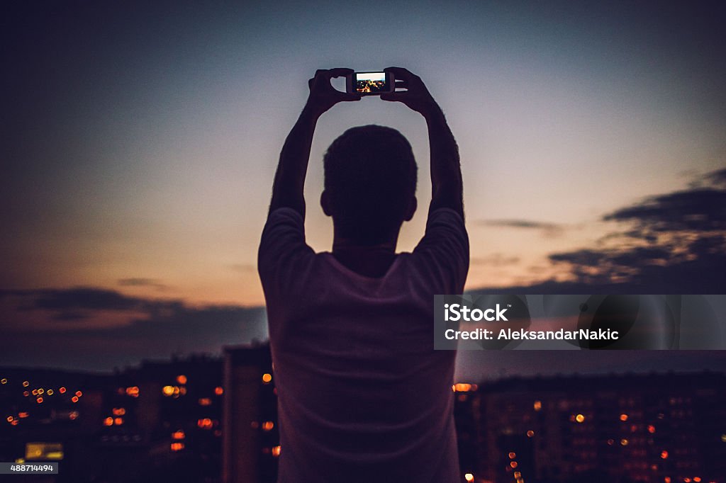 Photographing that perfect time of the day Young man is holding his mobile phone up above his head and capturing that perfect time of the day when sun is going down  Photographing Stock Photo