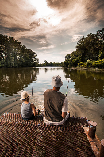 Rear view of a father and son fishing in freshwaters.