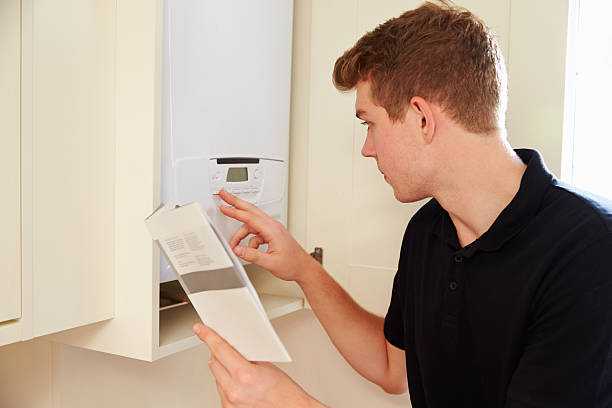 Young technician servicing a boiler, consulting manual Young technician servicing a boiler, consulting manual heating engineer stock pictures, royalty-free photos & images