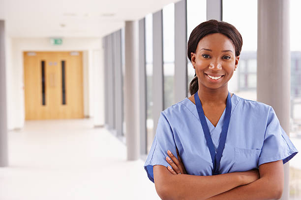 Portrait Of Female Nurse Standing In Hospital Corridor Portrait Of Female Nurse Standing In Hospital Corridor medical scrubs stock pictures, royalty-free photos & images