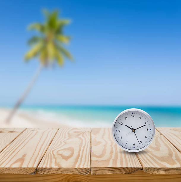 istock clock on wood table and blue sea background 488760130