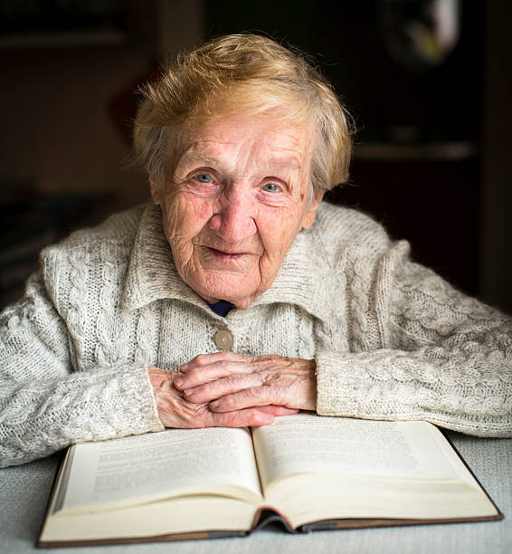 istock Grandmother sitting at the table with a big book. 488762932
