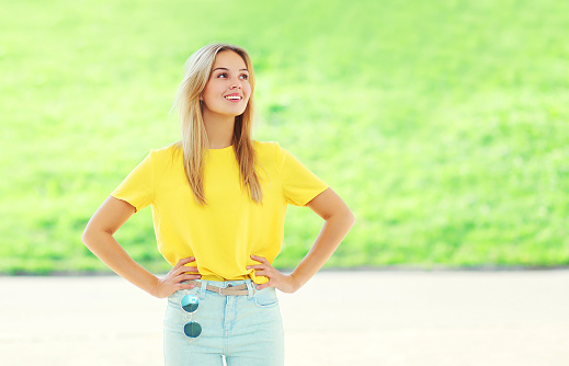 Beautiful smiling young woman wearing a colorful yellow t-shirt over summer grass background