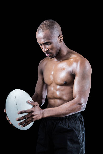 istock Concentrated shirtless athlete looking down while holding rugby ball 488766256