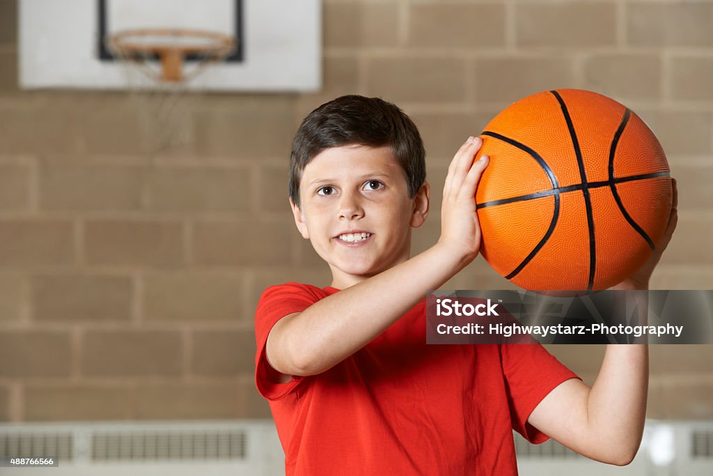 Boy Shooting durante el partido en la escuela Gimnasio de básquetbol - Foto de stock de Niños libre de derechos