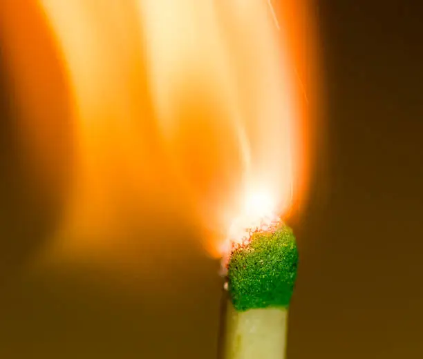 Close up of a green matchhead igniting against a dark background