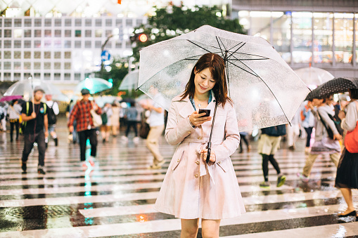 Japanese woman texting outside in the rain holding an umbrella.