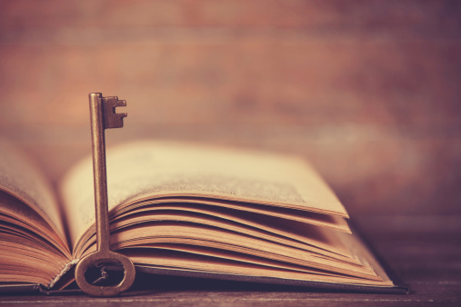 Retro key and opened book on wooden table.