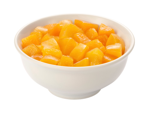 Diced Peaches in a white ceramic bowl, shown at an angle and in full focus from the front to the back.  This fruit is the cut up sections of the inside of a peach.  They float and thier own peach syrup.  They make a tasty side dish for any dinner, or can be served up as a snack.  They are considered a healthy and nutritious food.  Diced peaches are low in calories. The image is a cut out, isolated on a white background, with a clipping path.