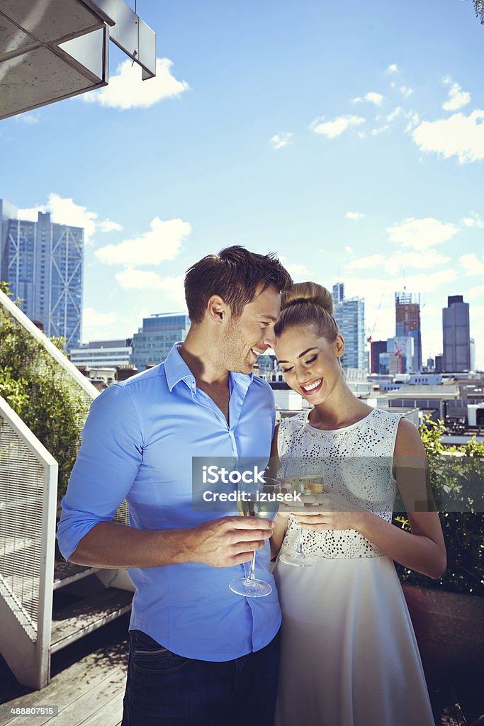 Romantic couple Outdoor portrait of affectionate couple standing with wine glasses on the terrace with cityscape in the background. Couple - Relationship Stock Photo