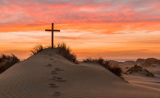 Black cross on a sand dune with foot steps leading up to it.