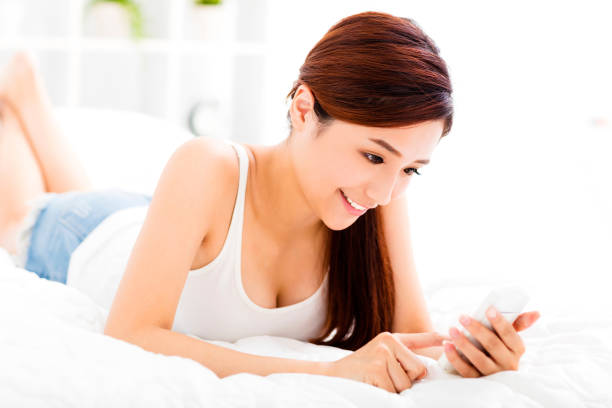 istock smiling young woman with smart phone on the bed 488821388