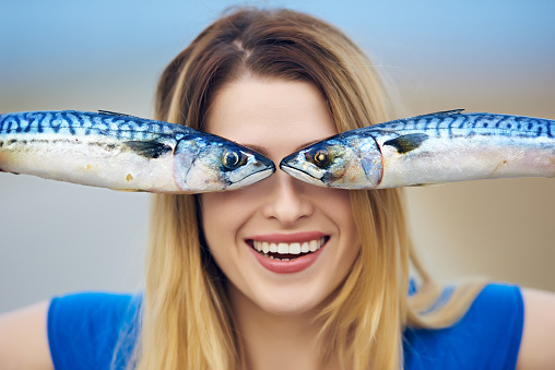 front view of woman portrait holding fishes in front of her eyes, smiling attitude.