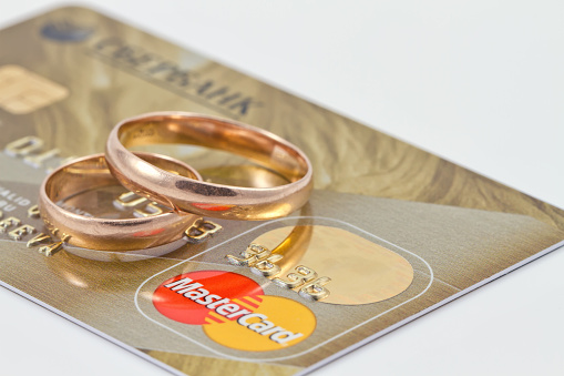 Volgograd, Russia - August 16, 2015: Gold wedding rings lie on a credit card payment system MasterCard gold on a background of money